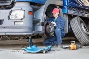 Mechanic in blue uniform kneeling beside blue truck, holding tool and hose changing a tire
