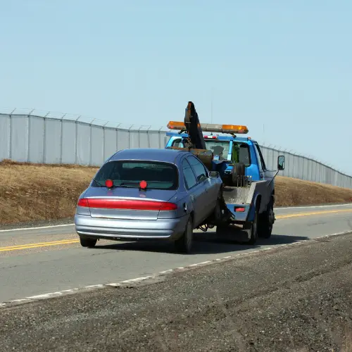 Blue tow truck towing silver car on road with fence and grassy area near maysiville, ky