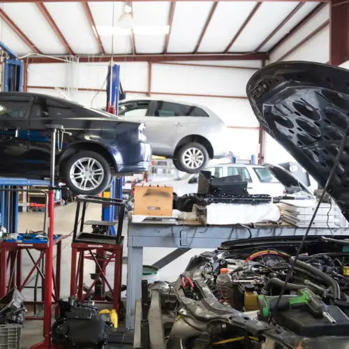 Cars on lifts and a mechanic working in a busy repair shop with tools, equipment, and an open-hood car.