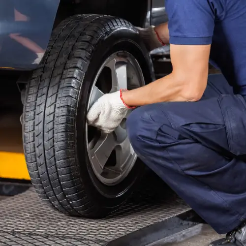 Person wearing gloves changes a car tire in an automotive shop, kneeling and securing the wheel.