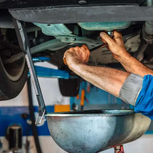 Mechanic draining oil from a car’s engine into a metal container in an automotive shop.