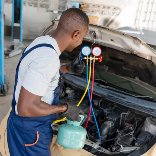 Mechanic in overalls refilling a car’s air conditioning system with coolant at an automotive shop using gauges and hoses.