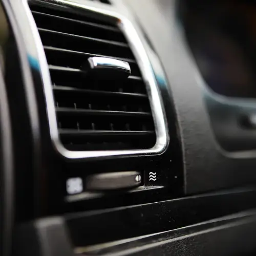 Close-up of a car’s air conditioning vent and control buttons on a black dashboard at a repair shop.