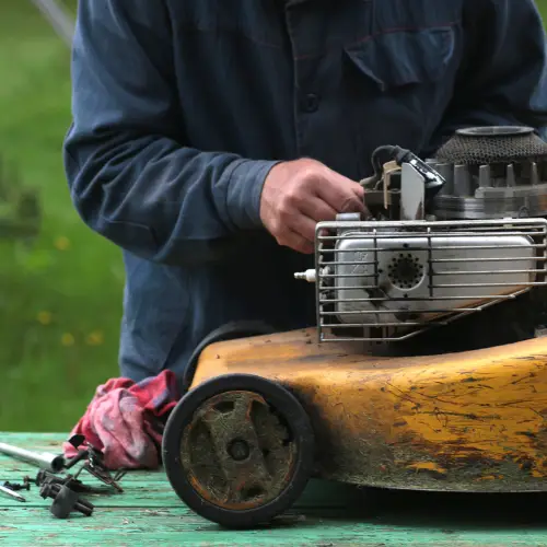 A mechanic repairs a yellow lawn mower on green grass, with tools and a red cloth nearby.