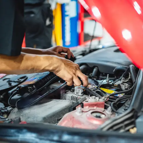 A mechanic’s hands working on a car engine in a brightly lit auto repair shop with the hood open.