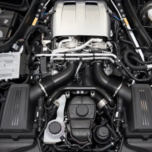 Close-up view of a modern car engine with various mechanical components and black plastic covers visible.