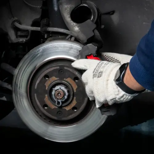 A person wearing gloves is inspecting or repairing a car brake disc and caliper.