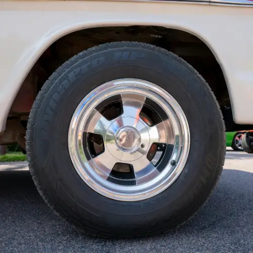 Close-up of a shiny chrome wheel and black tire on a white vehicle, parked on a paved surface.