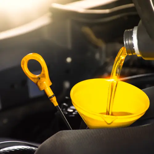 Engine oil being poured into a yellow funnel under a car hood, with a dipstick visible nearby.