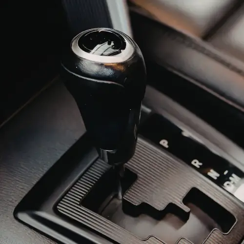 Close-up of a black automatic gear shift lever in a car, showing the gear positions on the console.